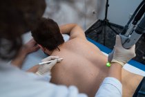 Unerkennbarer Meister mit modernem Laser auf dem Rücken des männlichen Klienten zur Haarentfernung in Schönheitsklinik — Stockfoto