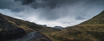 Pintoresco paisaje de ruta vacía rodeado de hierba seca y verde en terreno montañoso del Valle de Aran en España bajo un cielo gris nublado - foto de stock