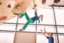Side view of strong female alpinist climbing wall in bouldering club under supervision of male instructor — Stock Photo