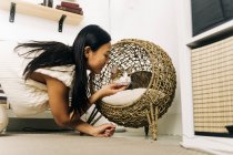 Vista laterale del raccolto allegro etnico femminile accarezzando affascinante gatto a riposo in casa di vimini — Foto stock