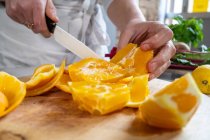 Erntehelferin schneidet reife saftige Orangen mit Messer auf Holzschneidebrett am Küchentisch — Stockfoto