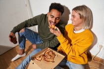 From above positive multiracial couple eating pizza slice together while having fun — Stock Photo