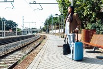 Seitenansicht einer asiatischen Reisenden mit Koffer, die auf dem Bahnsteig des Bahnhofs steht, während sie auf den Zug wartet — Stockfoto