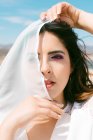 Young brunette woman covering eye with veil while looking at camera on wedding day — Stock Photo