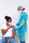 Жіночий медичний фахівець з захисної форми, латексні рукавички і особи з маскою вакцинують пацієнта афроамериканського чоловіка в клініці під час спалаху коронавірусу. — стокове фото