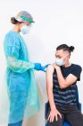 Female medical specialist in protective uniform, latex gloves and face mask vaccinating hispanic man patient in clinic during coronavirus outbreak — Stock Photo