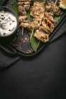 Von oben appetitlich frisch gekochtes Fleisch auf Spießen serviert auf Tablett auf schwarzem Tisch mit Schüssel mit Sauce — Stockfoto