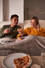 Pareja multiétnica sentada en sillones y comiendo deliciosa pizza mientras disfrutan del fin de semana juntos en casa - foto de stock