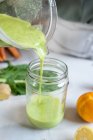 Ernte anonyme Frau gießt leckeren Smoothie aus Mixer-Schüssel in Glas am Tisch mit Zitrusfrüchten zu Hause — Stockfoto