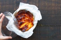 Von oben beschnitten bis zur Unkenntlichkeit peron mit köstlichen gebackenen Käsekuchen serviert auf einem Behälter in einem Holztisch — Stockfoto
