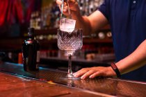 Unrecognizable bartender putting a big ice cube into the glass while preparing a gin tonic cocktail in the bar — Stock Photo