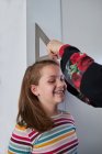 Неузнаваемый родитель с линейкой, измеряющей высоту веселой девушки, стоящей у стены в комнате — стоковое фото
