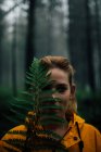 Viajero femenino adulto con hoja de planta verde exuberante mirando a la cámara durante el viaje en los bosques - foto de stock