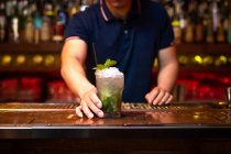 Hand of unrecognizable bartender gives you a well elaborated mojito cocktail in the bar after he finished to prepare it — Stock Photo