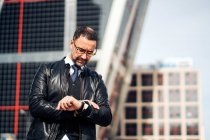 Serious mature Hispanic male executive in formal apparel and eyewear checking time on wristwatch in town — Stock Photo