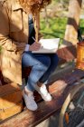 Crop of anonymous young thoughtful female taking notes in planner on wooden bench near bicycle in park in daytime — Stock Photo