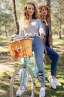 Full body of happy young girlfriends smiling and looking at camera on bicycle in sunny park in summer — Stock Photo