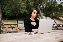 Empresária focada sentada à mesa com laptop no parque trabalhando remotamente — Fotografia de Stock