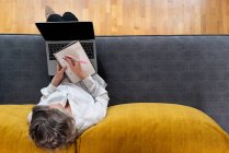 De cima anônimo trabalhador distância feminina com bloco de notas e caneta sentado no sofá contra netbook com diagramas na tela — Fotografia de Stock