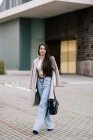 Молодая модная предпринимательница стоит у входа в современное здание в городе и смотрит в камеру — стоковое фото
