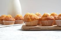 Délicieux muffins sucrés maison fraîchement cuits dans des tasses en papier disposées sur la table avec pot en verre de lait frais — Photo de stock