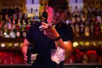 Jeune barman asiatique versant du gin du jigger au verre pour préparer un cocktail gin tonic au bar — Photo de stock