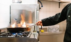 Side view of crop faceless cook preparing dish in frying pan on stove while working in kitchen of restaurant — Stock Photo