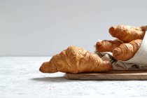 Croissants fraîchement cuits servis sur une planche à découper en bois avec serviette sur la table pour le petit déjeuner — Photo de stock