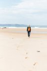 Вид ззаду на невизначену старшу жінку-похідницю, що йде на піщаному березі проти нескінченного моря під час подорожі — стокове фото