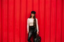 Щаслива жінка-підприємець в модному одязі, що стоїть на вулиці на фоні червоної стіни і дивиться на камеру — стокове фото