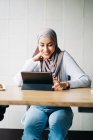 Содержание мусульманская женщина в хиджабе и говорить на видео чате через планшет, сидя за столом в кафе — стоковое фото
