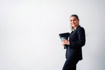 Позитивна середнього віку жінка-підприємець з хвостом у формальному костюмі, дивлячись на камеру, стоячи з папкою та чашкою напою на білому тлі — стокове фото