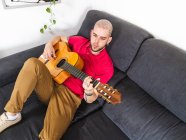 Músico pensativo em roupas casuais tocando guitarra na sala de luz em casa durante o dia — Fotografia de Stock