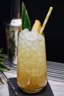 Жовтий коктейль у склянці, прикрашений ананасовим шматочком і зеленим листям з паперовою соломою, розміщеною на карнизі з барною ложкою — стокове фото