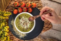 Vista aérea de la cosecha chef anónimo con tazón de deliciosa sopa de crema vegetariana con pistachos triturados y condimentos en la parte superior - foto de stock