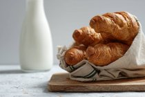 Délicieux croissants et bouteille de lait mis sur la table pour le petit déjeuner dans la cuisine — Photo de stock