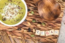 Top view of appetizing vegan cream soup with crushed pistachios on top on wicker mat with wooden spoon — Stock Photo