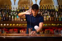 Молодий азіатський бармен наливає горілку в шейкер, готуючи коктейль у барі. — стокове фото