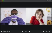 Concentrated young black male doctor in medical uniform and mask showing test tube with blood sample to attentive boy with earbuds patient during video call — Stock Photo