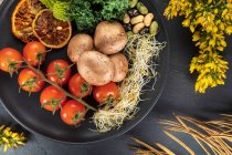 Вид сверху на тарелку со свежими помидорами вишни рядом с вареной картошкой и на фоне цветов — стоковое фото