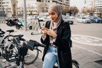 Vista lateral da mulher muçulmana em lenço de cabeça usando o sistema de compartilhamento de bicicletas na cidade — Fotografia de Stock