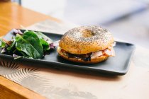 Appetizing bagel sandwich with cheese and chicken served on plate with rucola salad on table in cafe — Stock Photo
