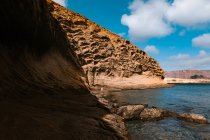 Reiserin steht während ihres Urlaubs in einem sonnigen exotischen Land an der Küste mit felsigen Klippen in der Nähe des reißenden Meeres — Stockfoto