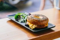 Sándwich de rosquillas con queso y pollo servido en el plato con ensalada de rúcula en la mesa en la cafetería - foto de stock
