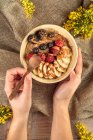 Вид сверху анонимного повара, показывающего миску с банановыми слайсами и ассорти свежих ягод с карамельным соусом на завтрак — стоковое фото
