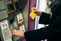 Side view of cropped unrecognizable female standing near ATM machine with card while buying train ticket while standing in modern terminal — Stock Photo