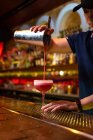 Jovem barman asiático trabalhando no bar com sua coqueteleira e derramando um coquetel no copo — Fotografia de Stock