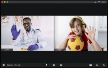 Happy little boy in headphones with ball in hand and young African American male doctor greeting each other with hand gesture while having video chat during online consultation — Stock Photo