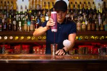 Jovem garçom asiático derramando suco de morango na coqueteleira enquanto prepara um coquetel no bar — Fotografia de Stock