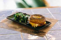 Appetitliches Bagel-Sandwich mit Käse und Huhn auf Teller serviert mit Rucola-Salat auf dem Tisch im Café — Stockfoto
